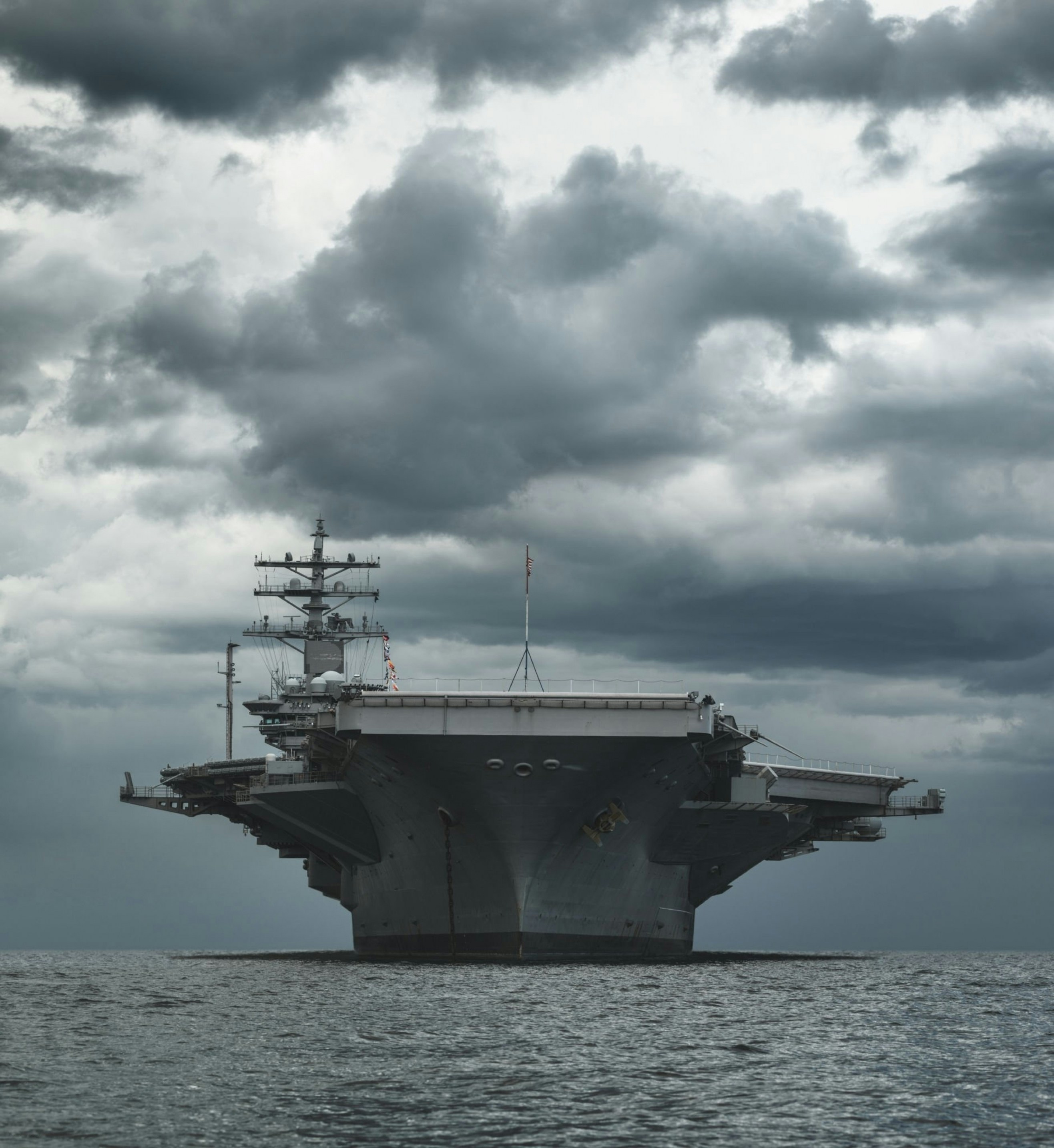 U.S. Navy aircraft carrier at anchor under heavy storm clouds at sea